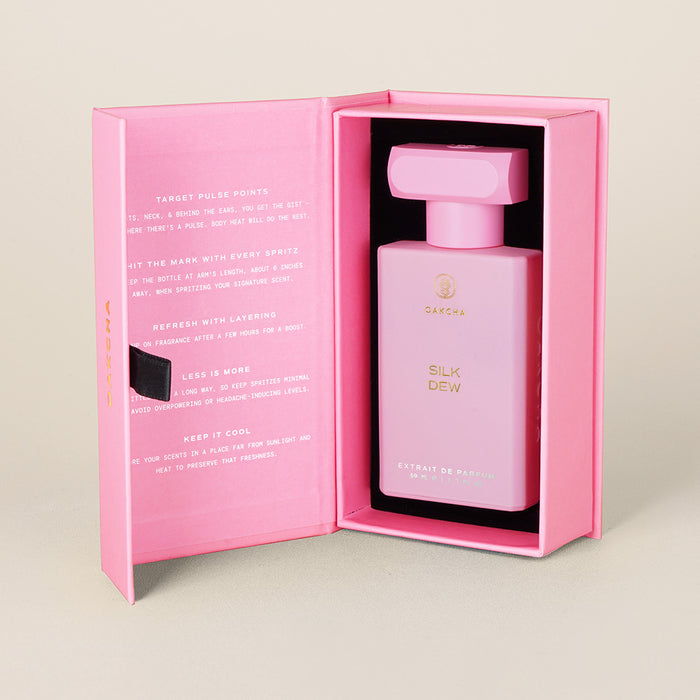 Three-quarter view of Silk Dew perfume in open pink box showing pink rectangular bottle and cap on beige background