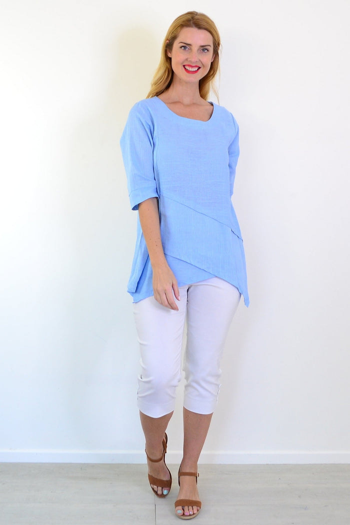 Sky blue layered linen blend tunic top by Ruby Rain, shown with flowing fabric and relaxed fit on a hanger.
