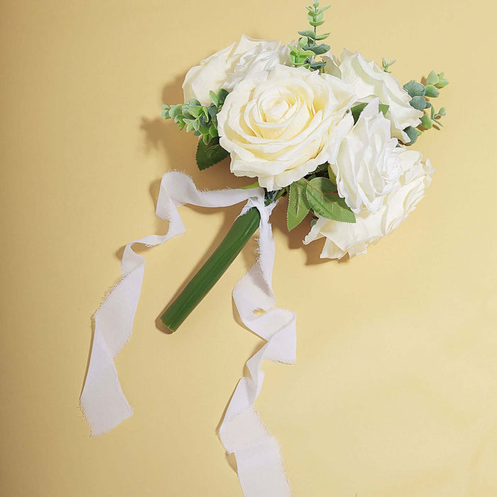 Artificial white rose bouquet with green accents and ribbon on a yellow background.