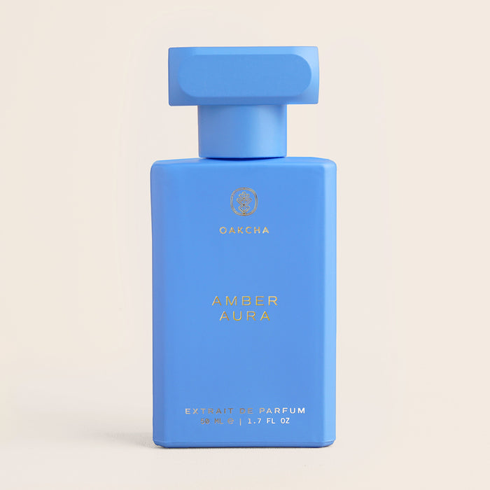 Front view of Amber Aura perfume bottle with matte blue rectangular body, gold logo, and square cap on beige background