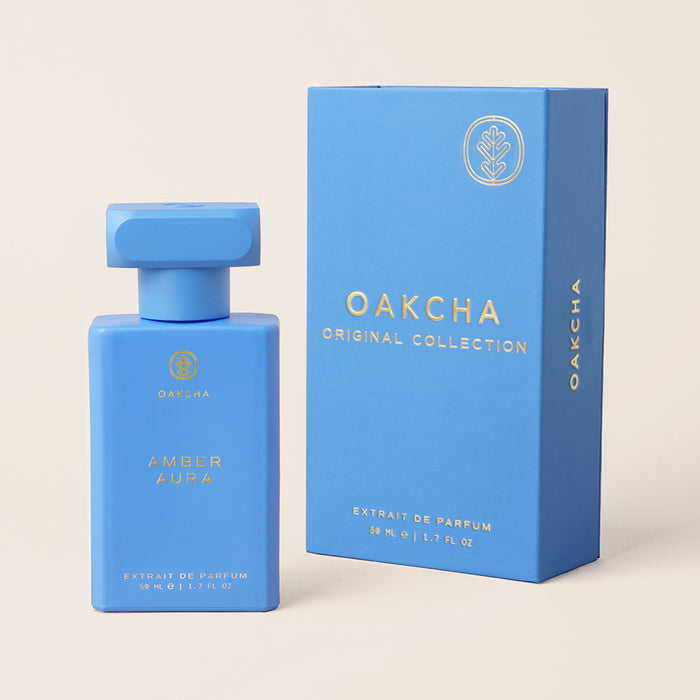 Front view of Amber Aura perfume bottle and matching box showcasing matte blue packaging with gold logo on a neutral background