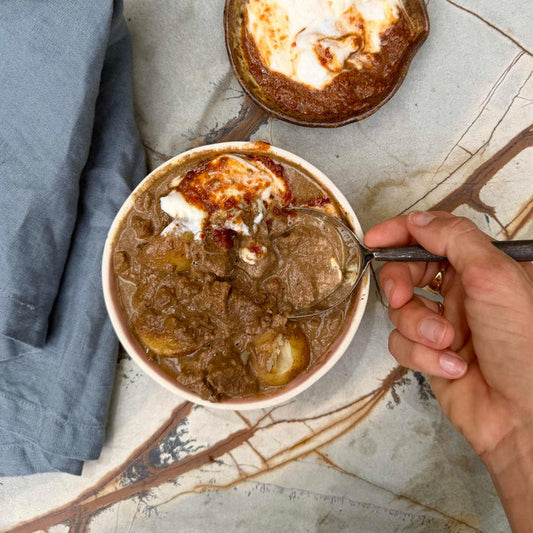 Hearty beef stew with potatoes and sour cream, ready meal served in a bowl with a spoon.