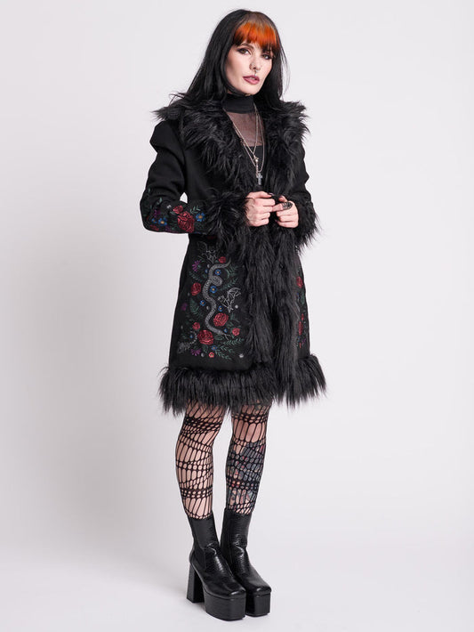 Woman wearing a black embroidered coat with feather details on a white background