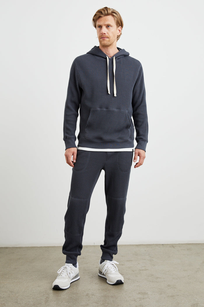 Cooper Waffle Thermal Pants with an Elastic Drawstring Waist, Two Teardrop Front Pockets, Two Back Welt Pockets, Reinforced Knee Patches and Elastic Cuffs in Ink Colorway - Front Full Body View Featured on Model