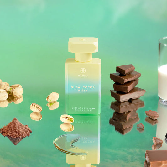 Angled view of Dubai Cocoa Pista bottle with gradient glass and gold cap beside pistachios and chocolate on teal surface