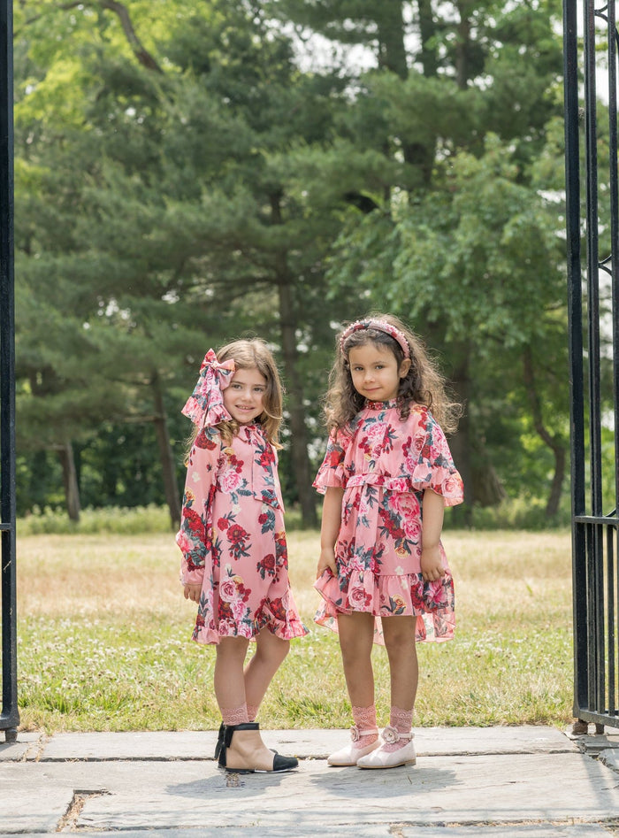 Two girls wearing coordinating pink floral outfits featuring the Flora flower print jumpsuit