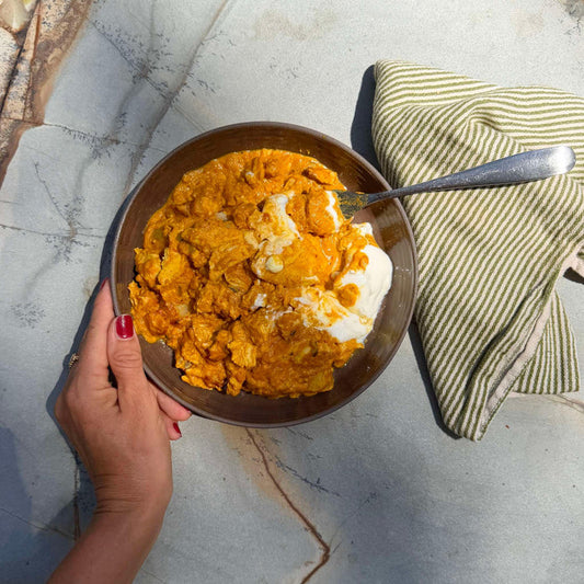 Creamy orange chicken curry with yogurt in a bowl, held over marble surface with striped napkin