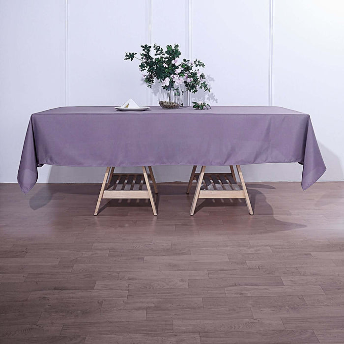 Purple tablecloth on a wooden table with a vase of flowers.