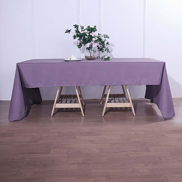 Purple tablecloth draped over a wooden table with a vase of flowers.