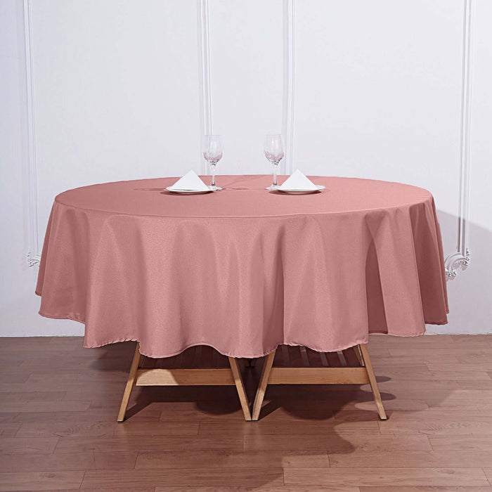 Round pink tablecloth draped on a wooden table with glasses and napkins.