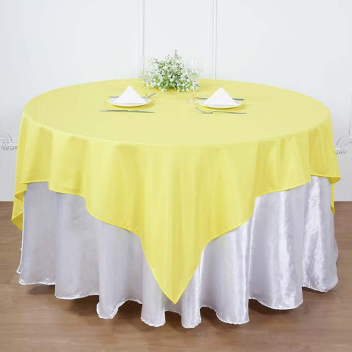Yellow round tablecloth draped over a silver tablecloth in a dining setup.