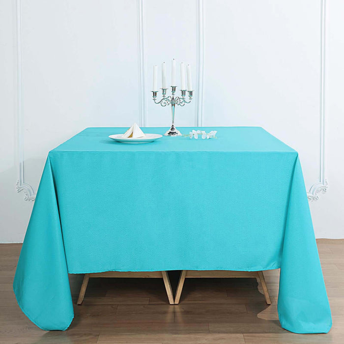 Turquoise tablecloth draped over a wooden table with candles and a plate.