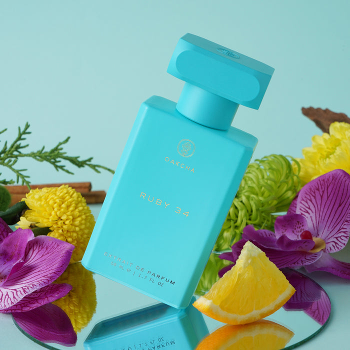 Angled view of Ruby 34 perfume bottle showing turquoise glass and gold label with orchids, yellow flowers and lemon wedge on blue background