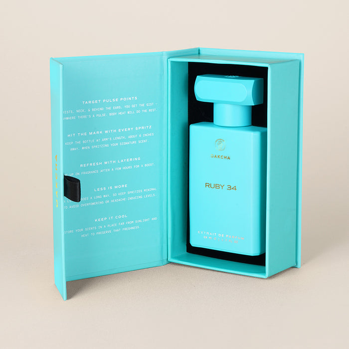 Front view of Ruby 34 perfume bottle in teal presentation box showcasing gold-foil logo and name with beige studio background