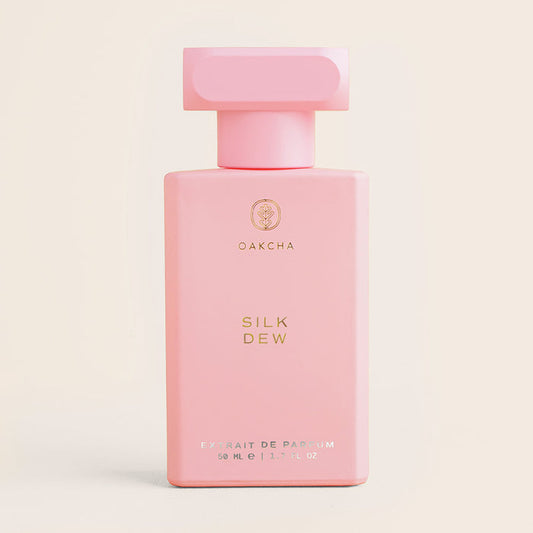 Front view of Silk Dew perfume bottle showcasing pale pink rectangular bottle with gold logo and matching cap on cream background