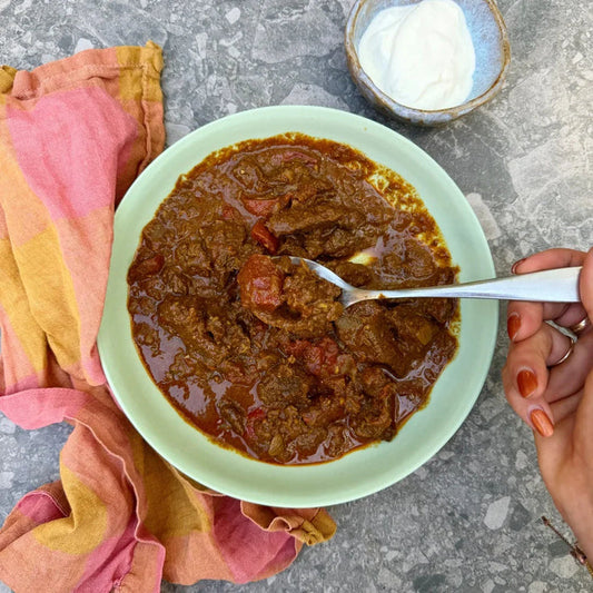 Rich beef curry with tomatoes in a green bowl, served with yogurt and a colorful napkin